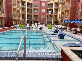 a swimming pool at an apartment building with chairs and umbrellas